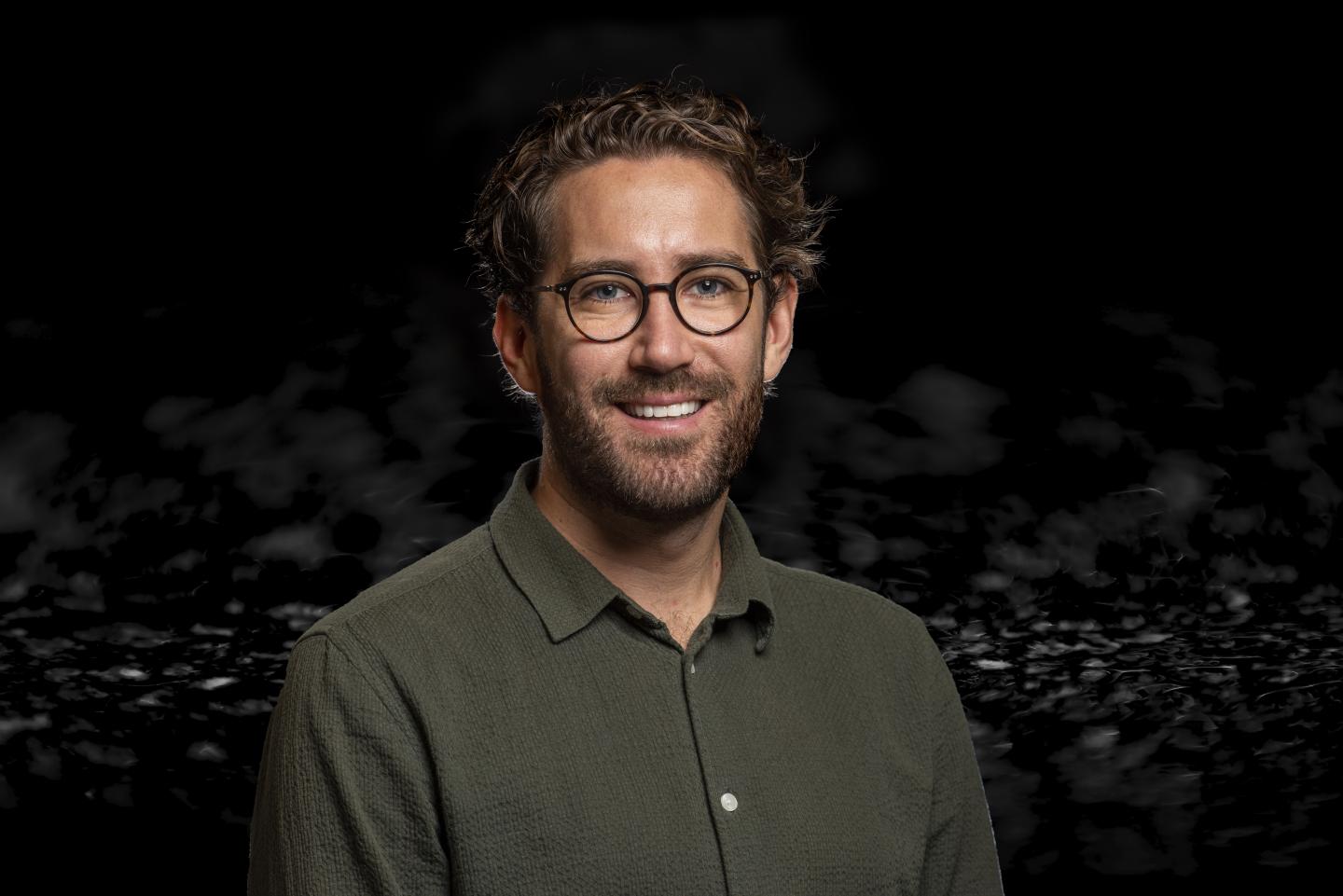 Porträtt av Filip Fagerström på Wapros inköpsavdelning, leende med glasögon och grön skjorta mot mörk bakgrund Porträtt av Filip Fagerström på Wapros inköpsavdelning, leende med glasögon och grön skjorta mot mörk bakgrund