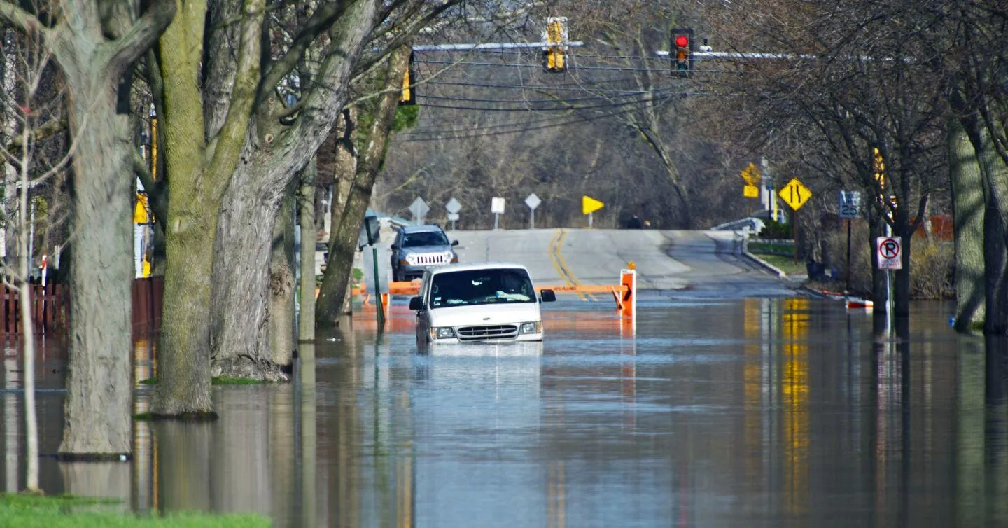 Car driving along a flooded road lined with trees and traffic lights, illustrating the financial effects of flooding