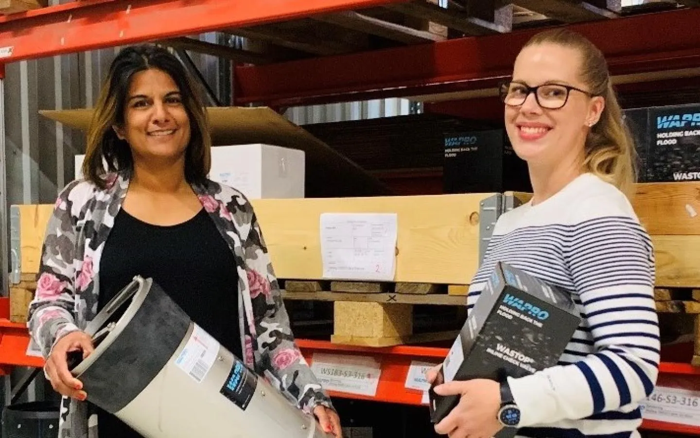 To medarbejdere fra Wapros kundeservice på lageret holder en WaStop kontraventil og en WaStop emballage To medarbejdere fra Wapros kundeservice på lageret holder en WaStop kontraventil og en WaStop emballage