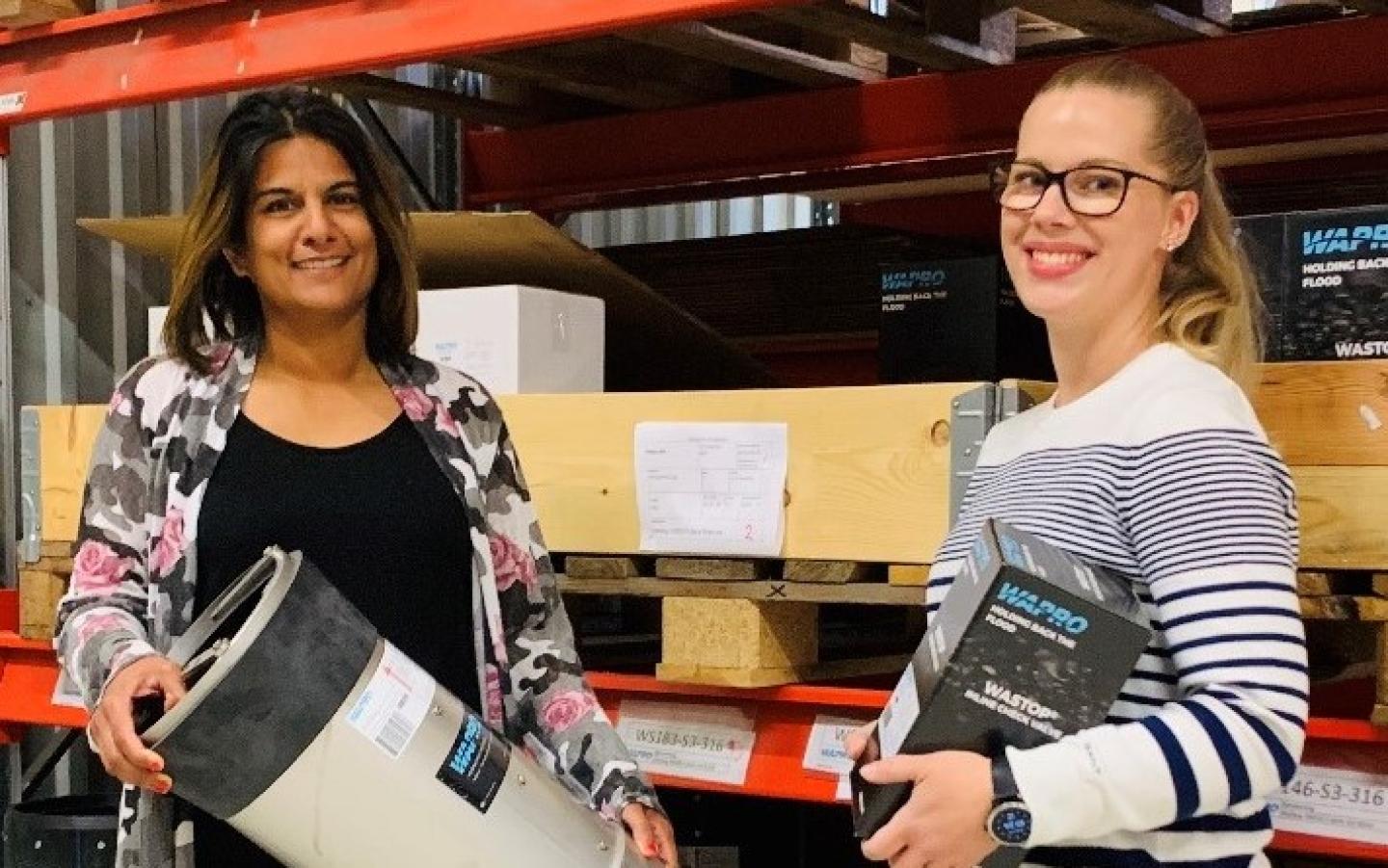 Två medarbetare från Wapros kundservice i lagret håller en WaStop backventil och en WaStop-förpackning